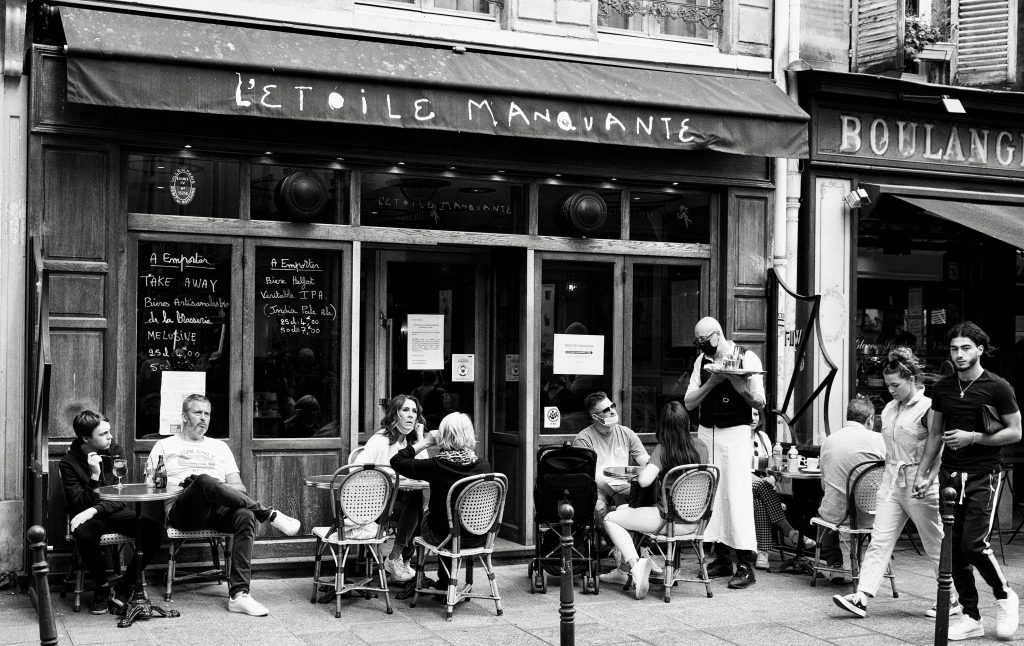 Black and white photo capturing vibrant street life at a Parisian cafe with people enjoying their time.